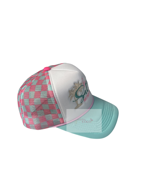 side view of hat. Pink and teal checkered trucker hat featuring embroidered ‘be salty,’ a beige palm tree, and the Bible verse Matthew 5:13 on the front panel