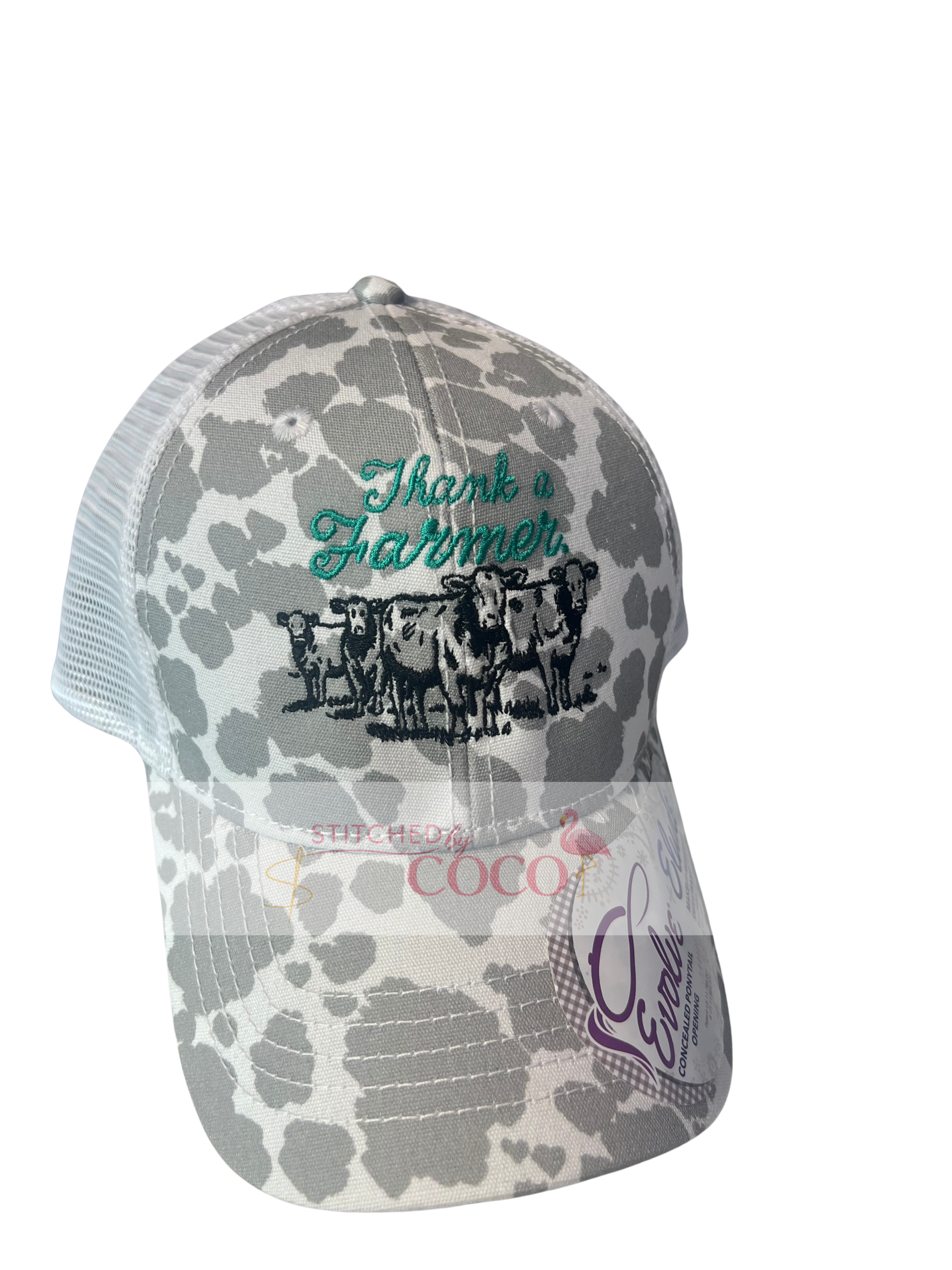 “Women’s gray and white cow‑print baseball hat featuring green ‘Thank a Farmer’ embroidery above a detailed black stitched cow graphic on the front.